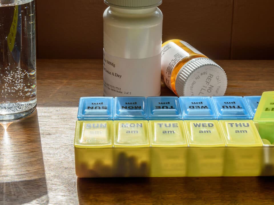 image of a pill bottle and organizer on a table beside a glass of water for a patient who wonders how blood pressure medication affects your oral health