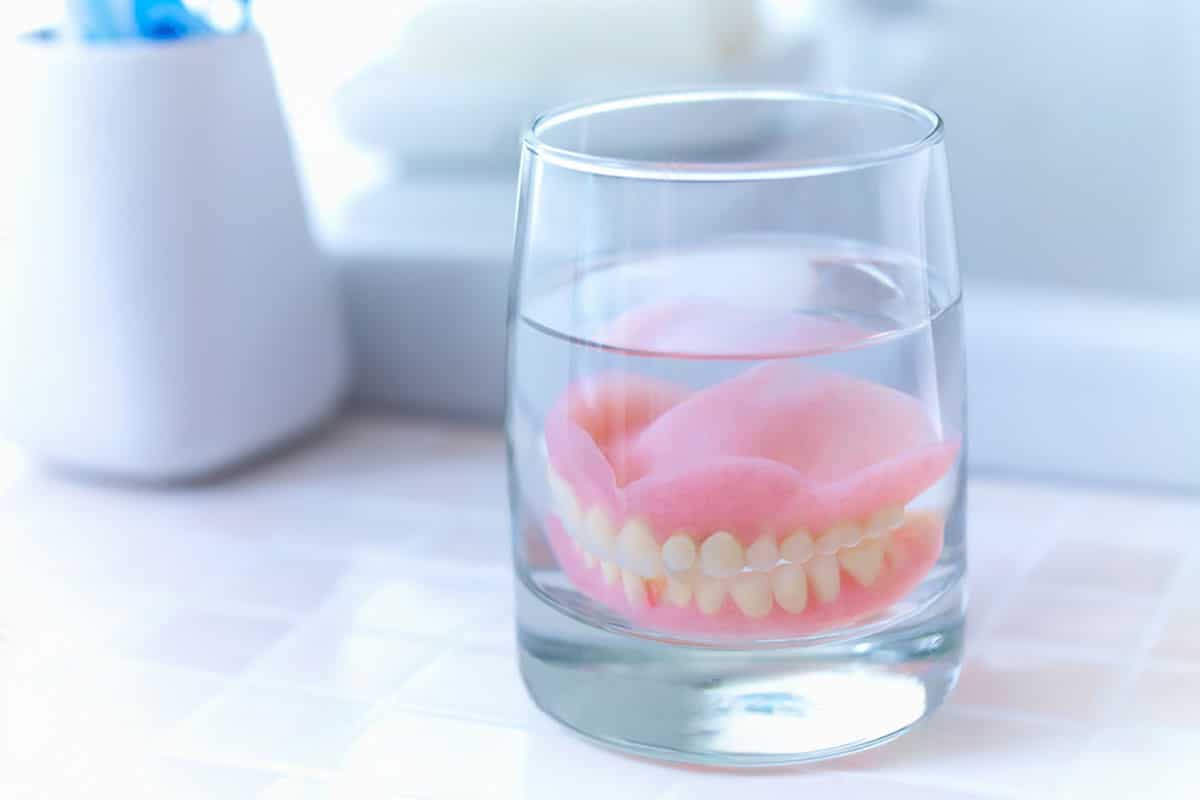 a set of dentures are being cleaned in a glass of water and cleaning solution.