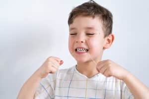 photo showing a young boy using dental floss after his mom asked her dentist "do toddlers need to floss?"