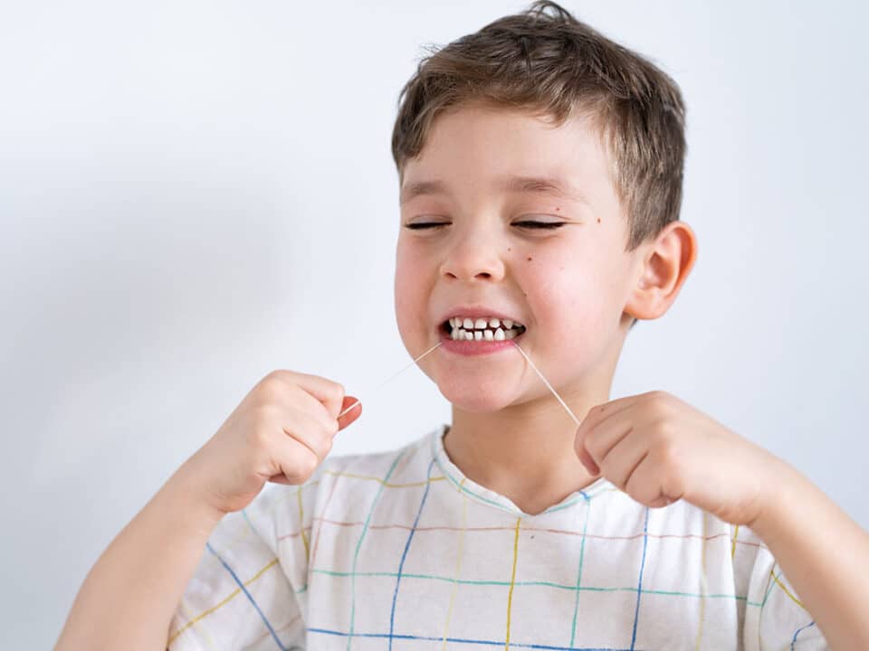 photo showing a young boy using dental floss after his mom asked her dentist "do toddlers need to floss?"