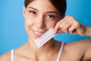 smiling woman holds up a set of strips and wonders if at-home teeth whitening strips work?