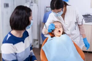 mother watches as pediatric dentist examines her daughter for signs of gingival hyperplasia in children and overgrown gums