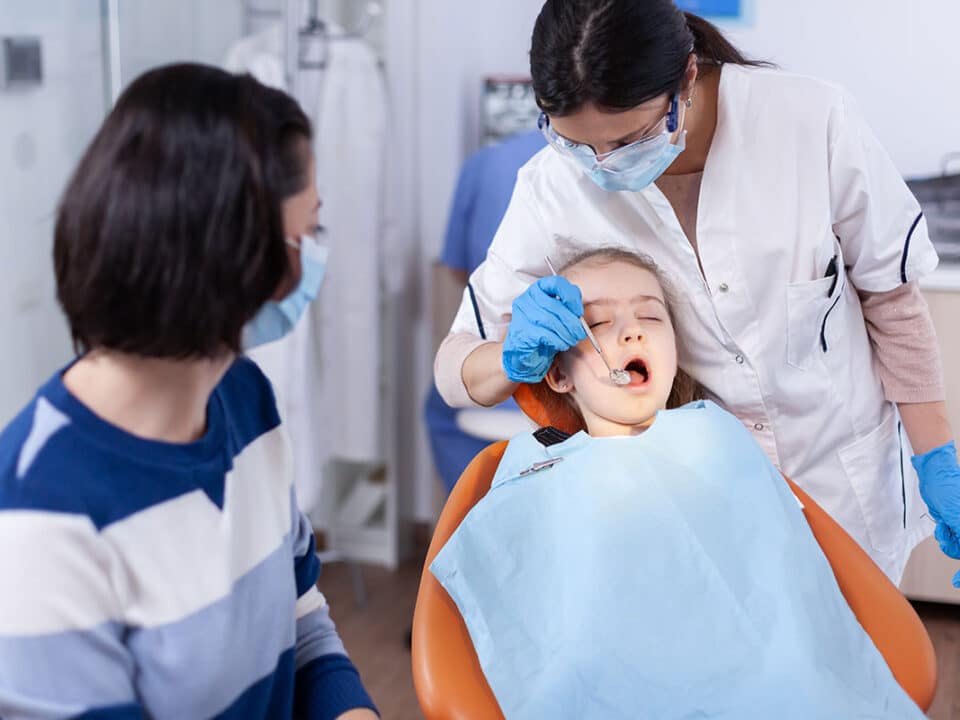 mother watches as pediatric dentist examines her daughter for signs of gingival hyperplasia in children and overgrown gums