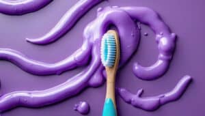 image showing purple toothpaste on a purple background with a blue toothbrush as the featured image for an article comparing pap+ and purple toothpaste as peroxide whitening alternatives