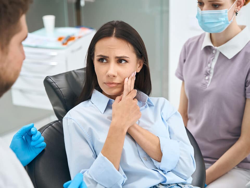 woman with toothpain holds her mouth while asking her dentist, "can a tooth be saved from extraction?"