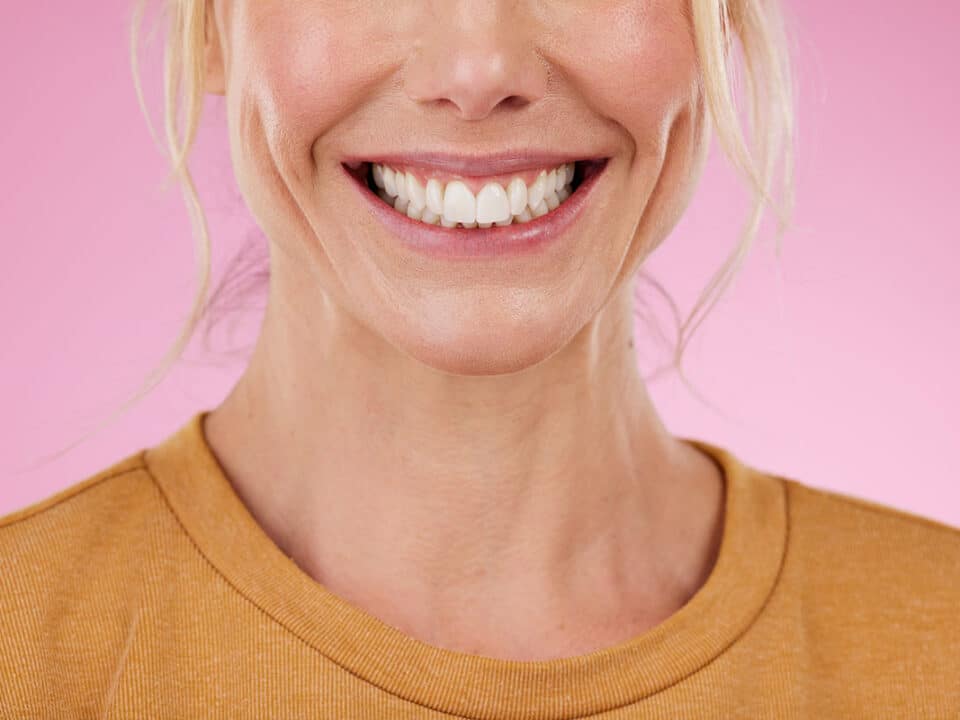 photo of a woman smiling and showing off her perfect smile against a pink background