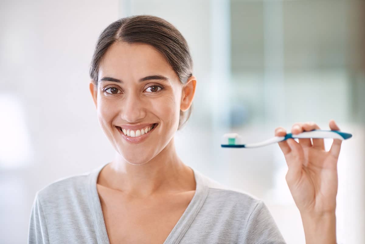 brunette woman holda a toothbrush in her hand as she wonders can gum recession be reversed.