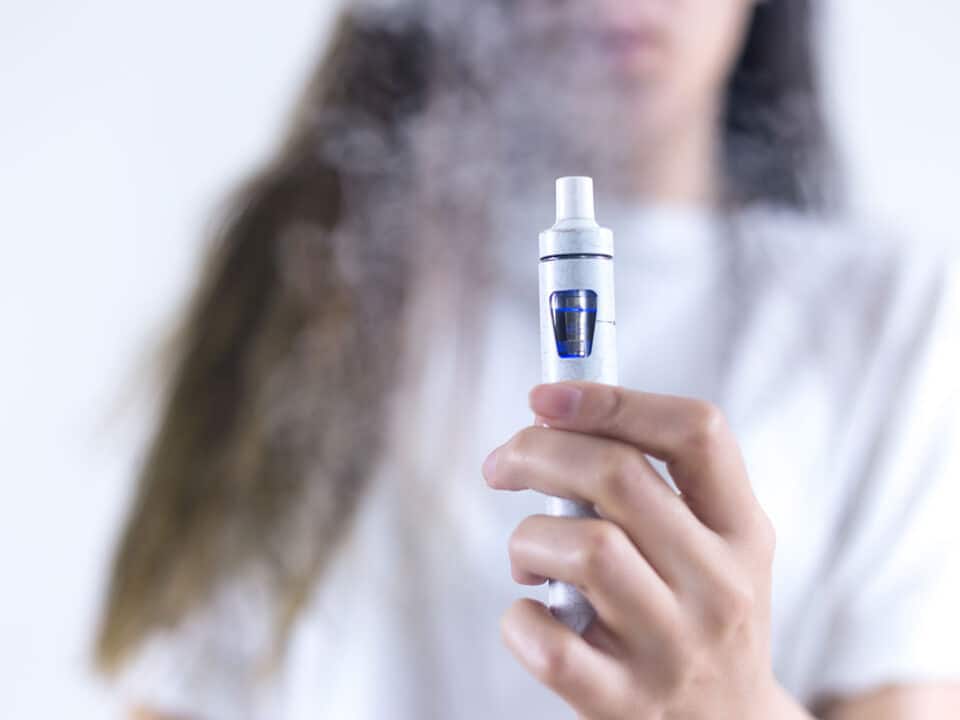 a woman holds out a vaping device as she wonders if vaping is bad for your oral health