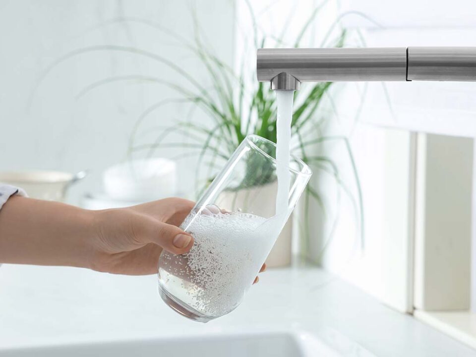 woman is filling glass of water in her sink as she wonders is Hamilton tap water fluoridated
