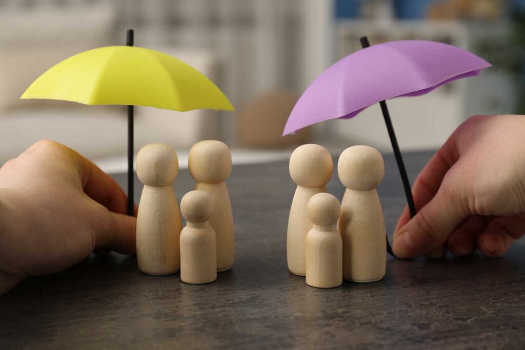 an image of some wooden figurines clustering under two umbrellas to signify the comparing odsp to ontario works and cdcp dental coverage