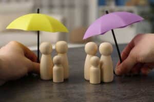 an image of some wooden figurines clustering under two umbrellas to signify the comparing odsp to ontario works and cdcp dental coverage