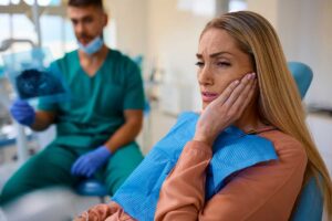 woman in an orange sweater holds her cheek in pain but feels thankful that she found the help of an emergency dentist in hamilton that can help her