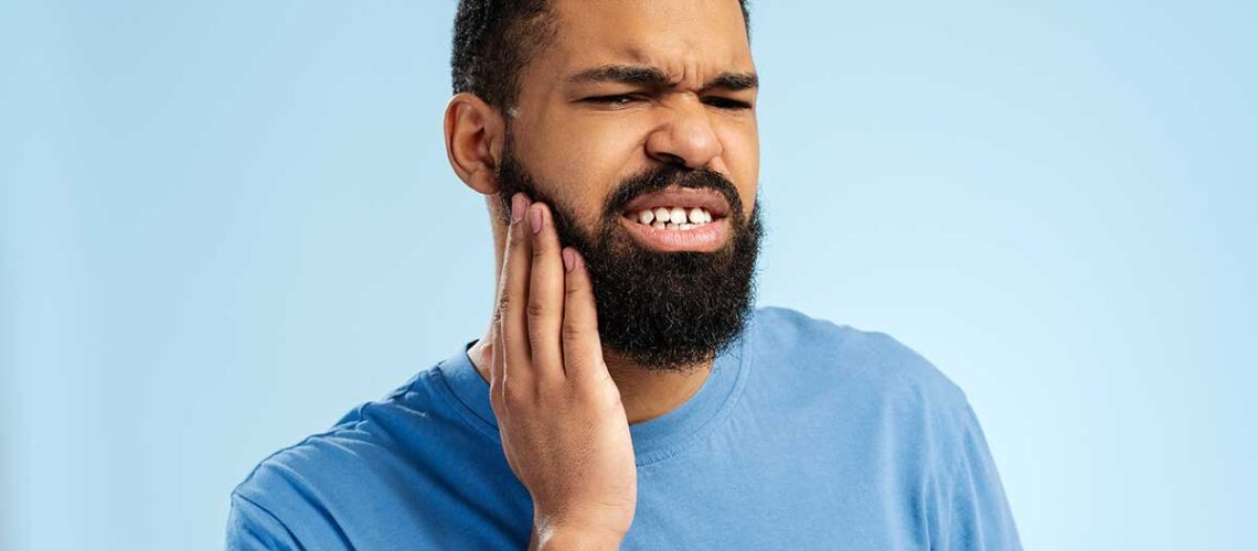 man with a big beard holds his face as an apparent toothache hits