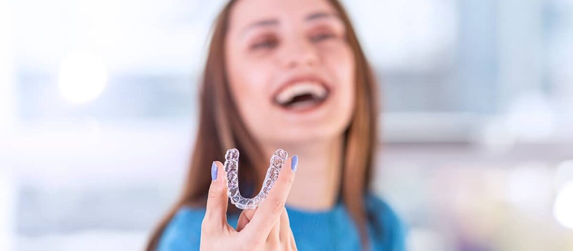 woman is laughing and smiling as she holds her new clear braces