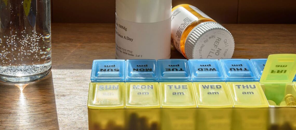image of a pill bottle and organizer on a table beside a glass of water for a patient who wonders how blood pressure medication affects your oral health