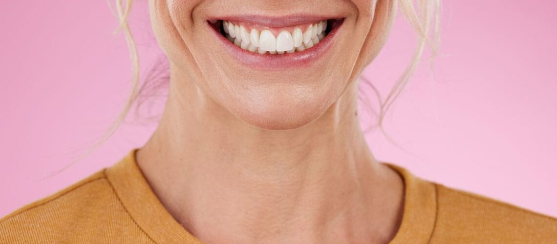 photo of a woman smiling and showing off her perfect smile against a pink background