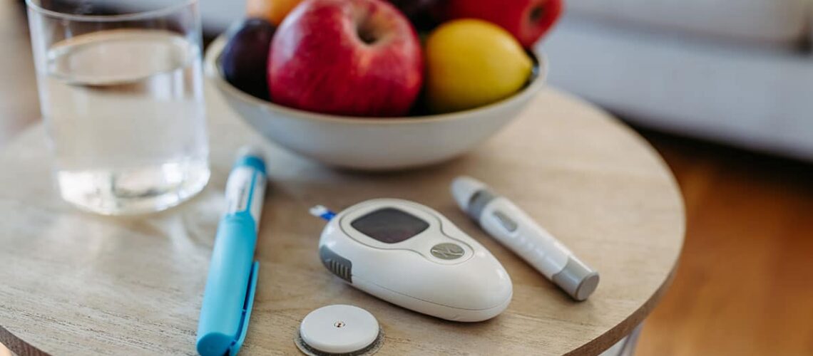 featured image of the diabetes and oral health article shows an insulin needle, a blood sugar monitor and some fruit on a table
