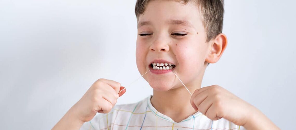 photo showing a young boy using dental floss after his mom asked her dentist "do toddlers need to floss?"