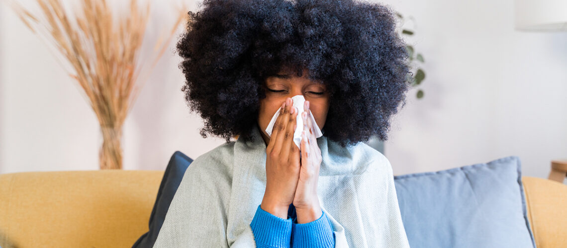 woman with a big fro blows her nose while sitting on a couch