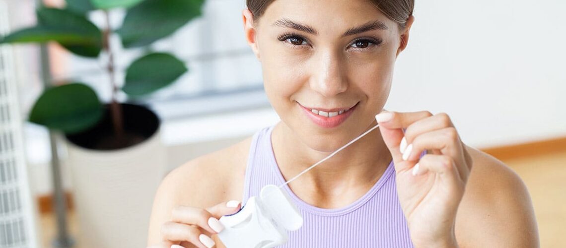 woman smiling as she holds a container of floss and debates - floss vs waterpik, which is better?
