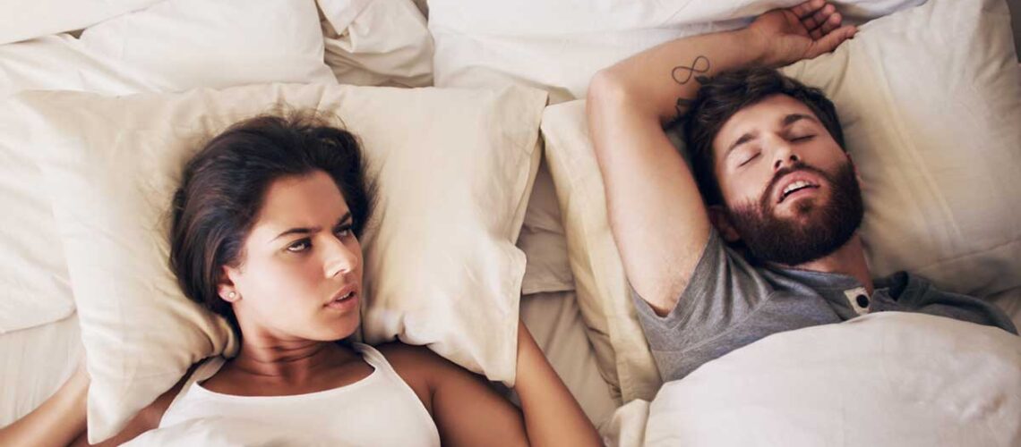 couple in bed and the woman is looking at her man angrily because he's snoring due to his untreated sleep apnea