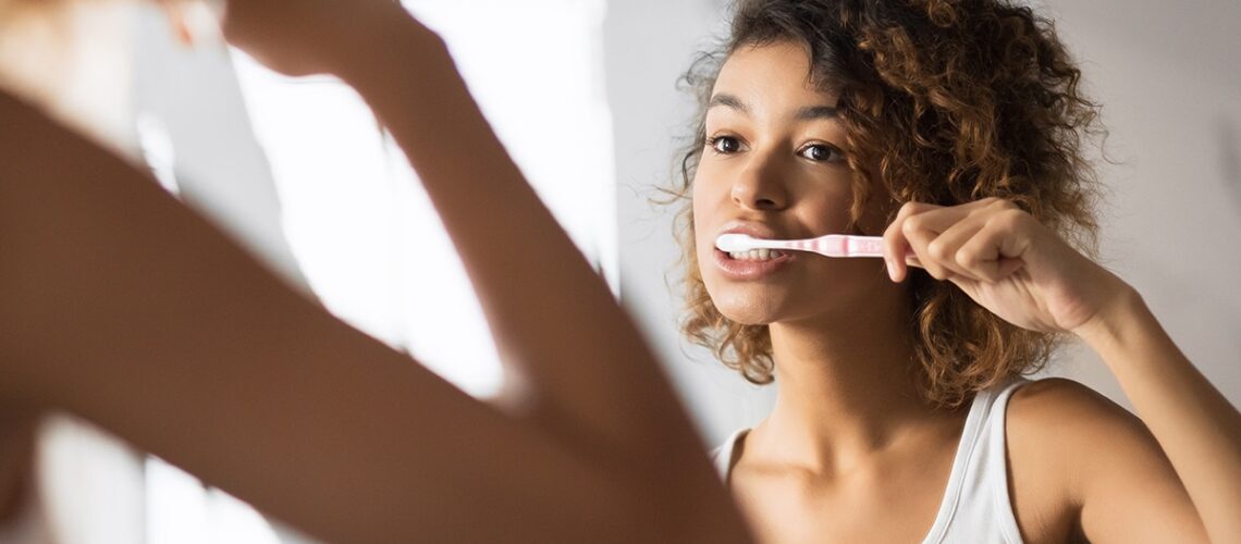 young woman stands in front of the mirror brushing her teeth properly