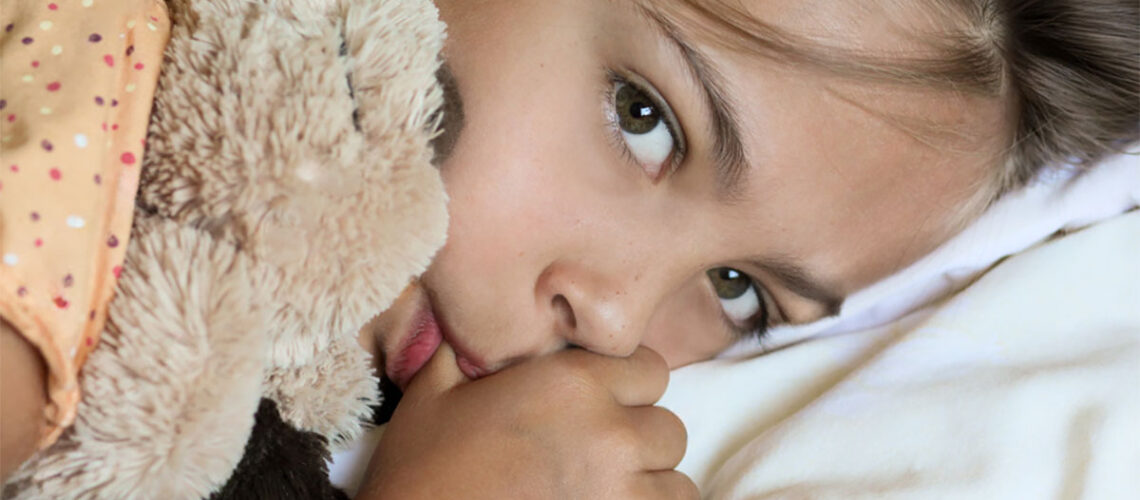 photo shows a young girl holding her teddy bear while sucking her thumb as she wonders how to stop thumb sucking