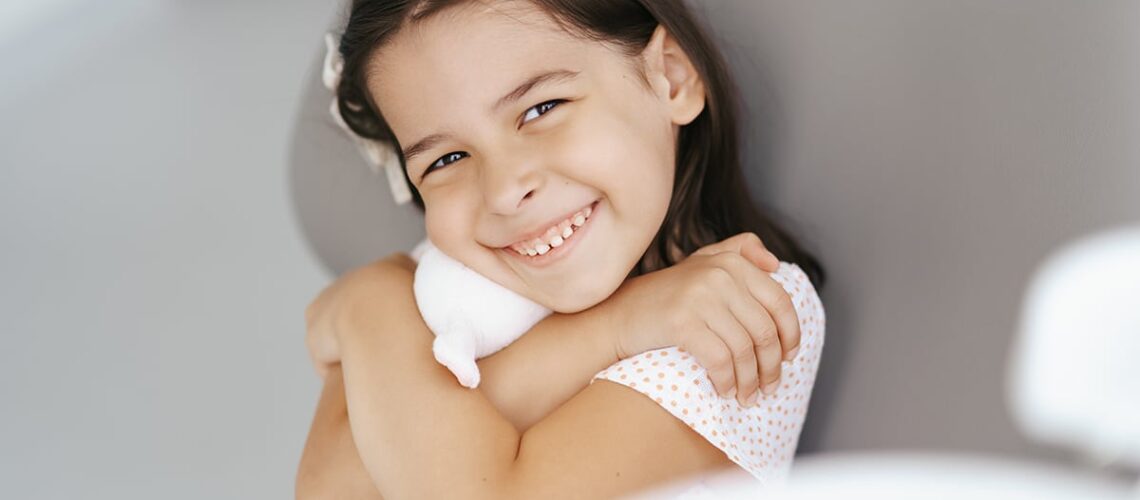 young girl is happy holding her toy bunny rabbit at the dentist because her parents prepared her properly