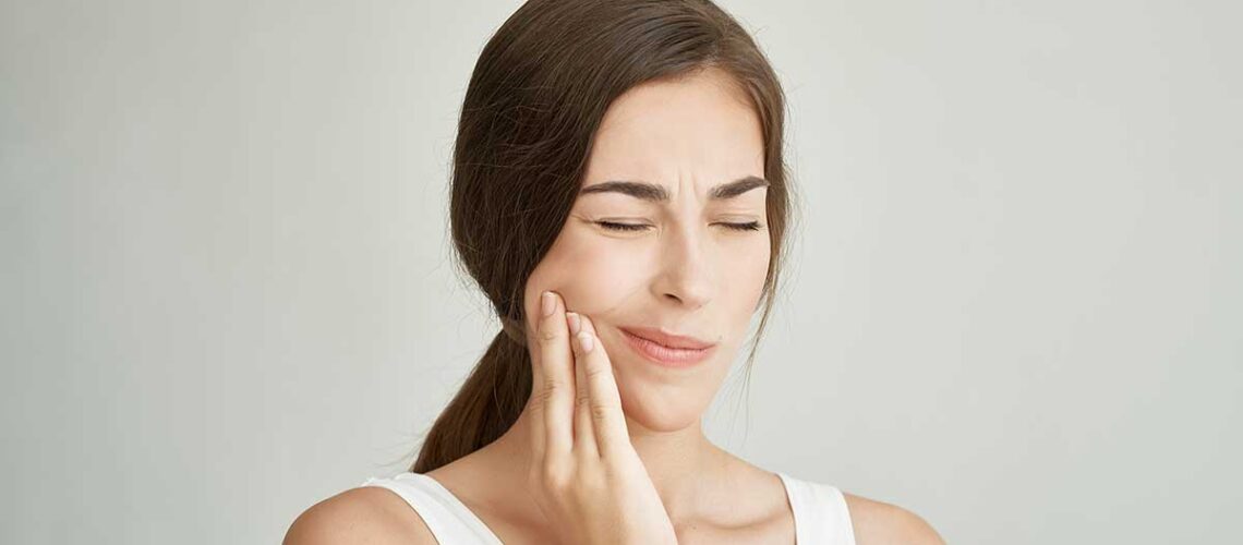 photo of a woman in a white tank top holding her jaw in pain