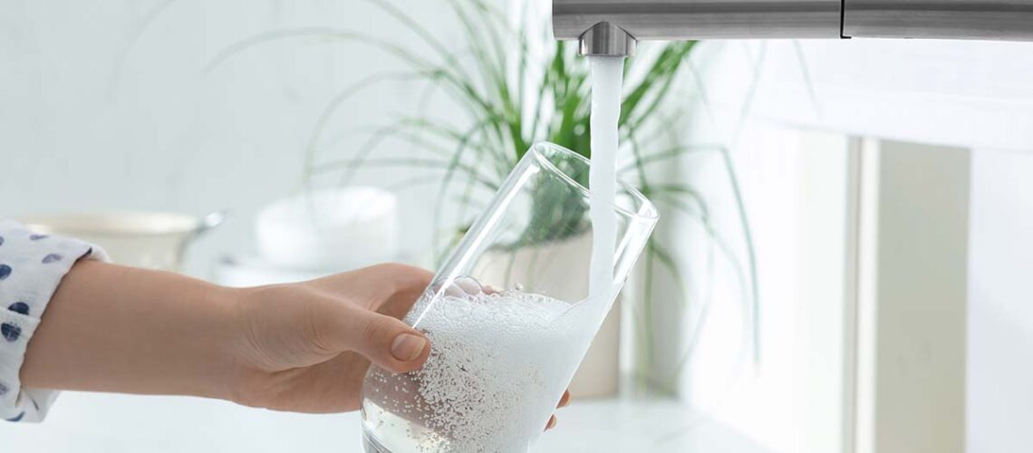 woman is filling glass of water in her sink as she wonders is Hamilton tap water fluoridated