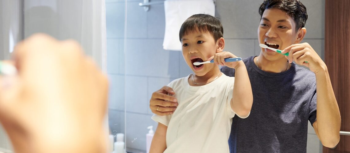 father and son brush their teeth together in the mirror