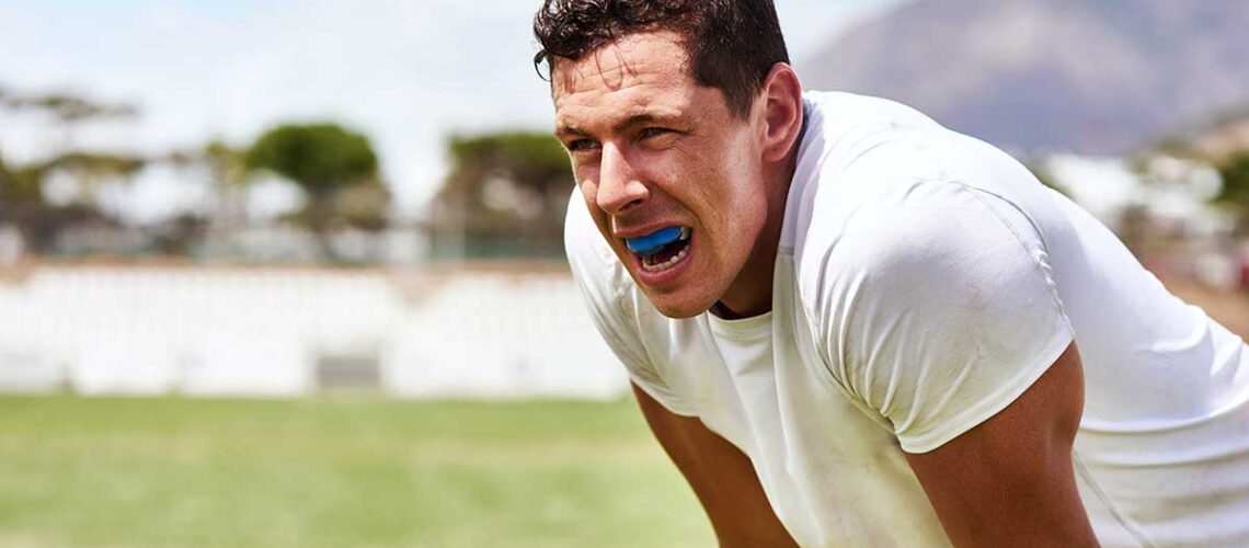 sweaty athlete bent over breathing hard showing off the mouthguard that is protecting his teeth and preventing sports related dental injuries