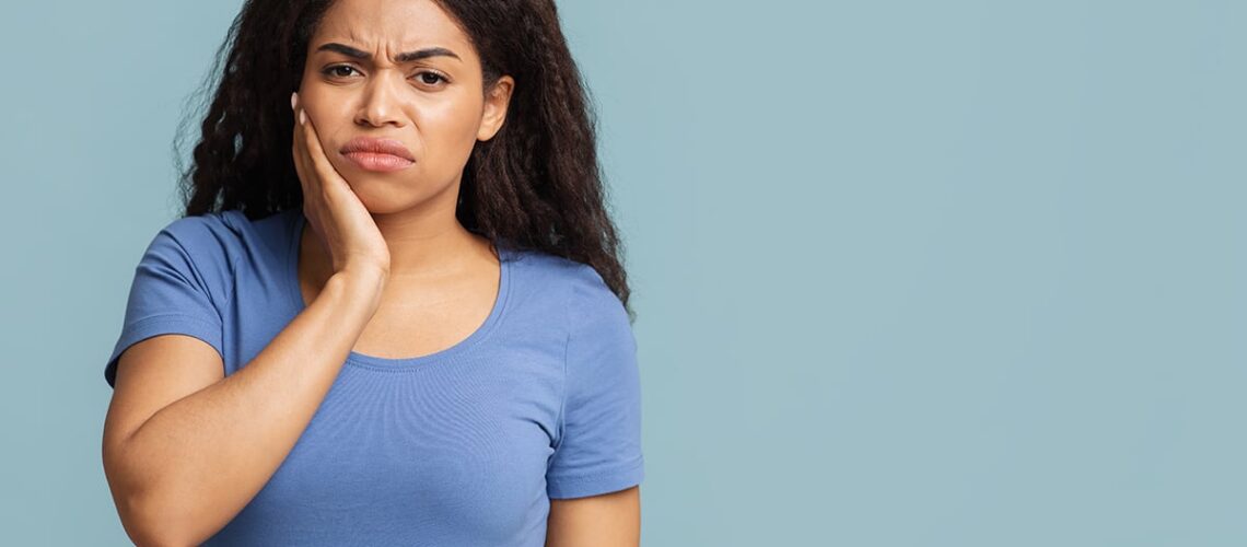 woman in a blue shirt holds her face as she experiences one of the painful symptoms of an abscessed tooth