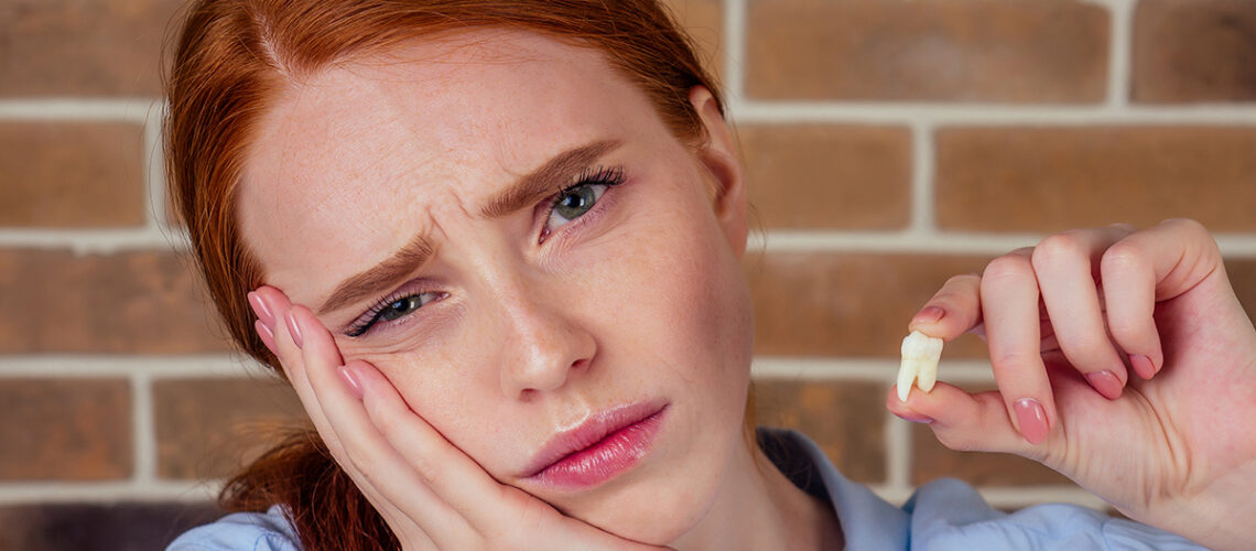red haired woman looks upset as she holds a tooth as she needs tips to fend of periodontal disease
