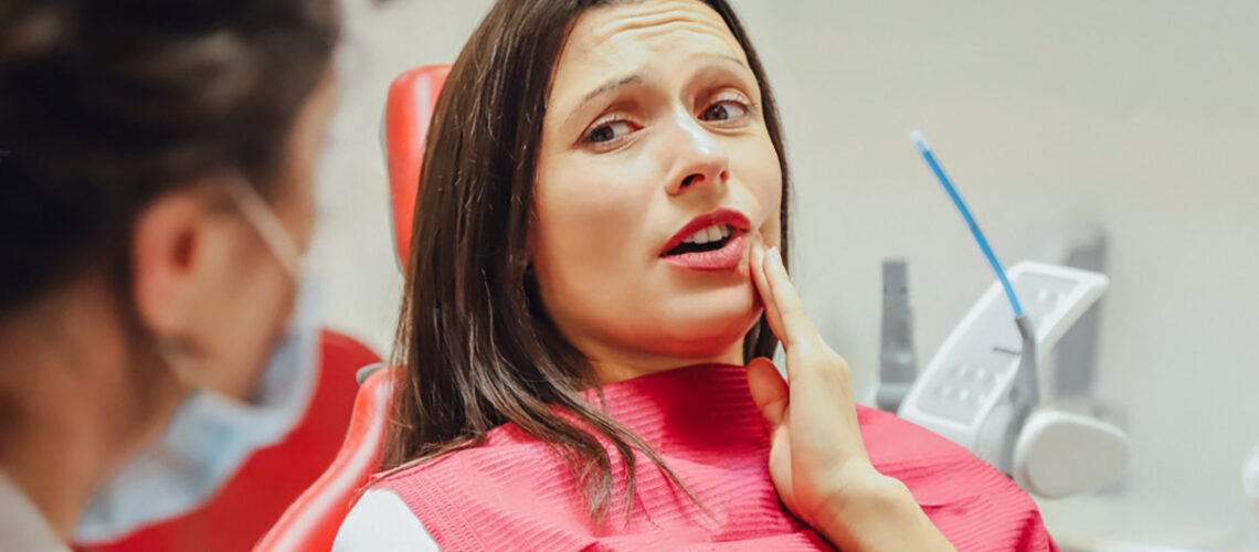 woman touches the side of her face as she speaks with her dentist about what to expect during a root canal treatment