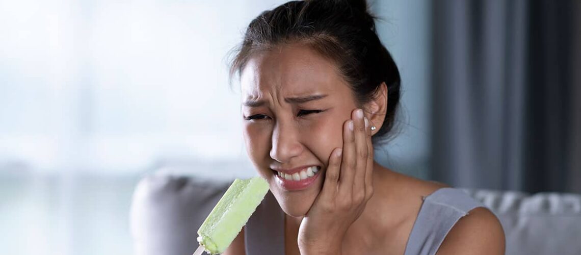 asian woman hit by tooth pain while eating a popsicle, so she wonders "why are my teeth sensitive?"